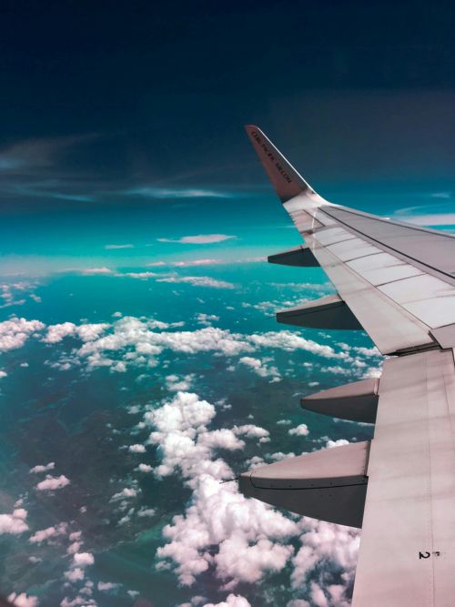 View from an airplane window showing the wing, clouds, and landscape far below.