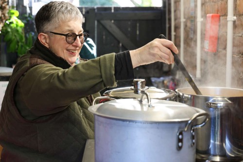 Person stirring soup in a large pot in a kitchen.