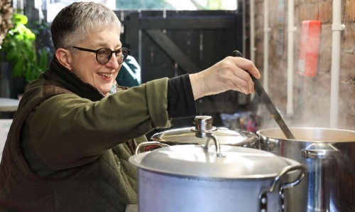 Person stirring soup in a large pot in a kitchen.