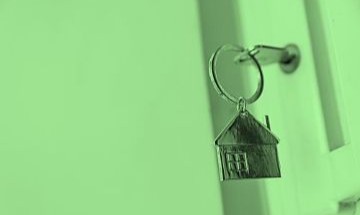 A house-shaped keyring hanging from a key in a door lock.